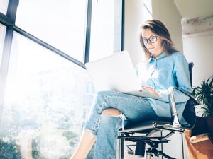 Digitalisierung: Eine Frau sitzt mit ihrem Laptop vor einer großen Fensterwand